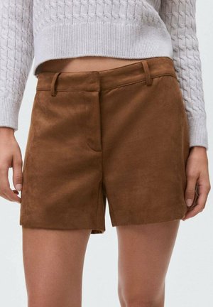 Shorts en faux suède marron avec une texture lisse, dotés de poches avant et d'une taille ajustée. Associés à un pull en maille gris clair.