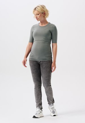 Stilltop in olivgrün, eng anliegendes Design mit kurzen Ärmeln. Kombiniert mit grauen Jeans aus Denim, die eine schmale Passform und eine dezente Textur aufweisen.