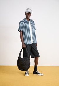 Cămașă cu dungi alb-albastră, pantaloni scurți negri, geantă neagră matlasată, șapcă gri și pantofi sport negri cu tălpi albe, pe o podea galbenă.