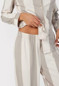 Set di pigiama leggero a righe beige e bianche, con una maglietta con bottoni e taschino sul petto e pantaloni con cintura elastica.