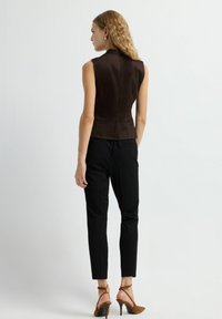 Brun satin uden ærmer med høj krave, parret med sorte skræddersyede bukser og brune højhælede sandaler med remme. Glat tekstur, tætsiddende design.