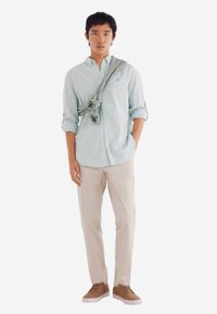 Lichtblauwe gestreepte blouse, beige broek en bruine sneakers. Een grijze trui is over de schouder geknoopt. Eenvoudige, casual outfitindeling.