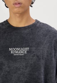 Tummanharmaa collegepaita pehmeästä kankaasta. Siinä on pyöreä pääntie ja valkoinen painettu teksti "MOONLIGHT ROMANCE KAOTIKO SOCIETY" edessä.