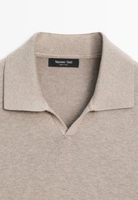 Beige strikket poloshirt med ribbet krave og åben halsudskæring, med en "Massimo Dutti" label indeni kraven.