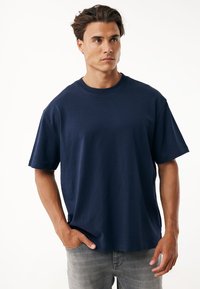 Camiseta de algodón azul marino con un corte holgado, mangas cortas y escote redondo. Presenta un diseño minimalista sin logotipos ni patrones visibles.