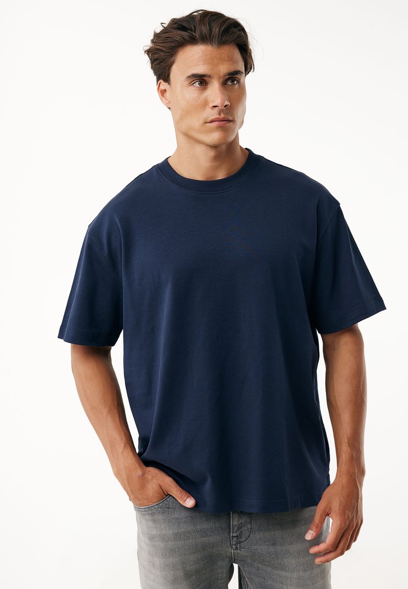 Camiseta de algodón azul marino con un corte holgado, mangas cortas y escote redondo. Presenta un diseño minimalista sin logotipos ni patrones visibles.