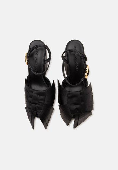 Paire de sandales noires à bout ouvert avec un design avant superposé et plié, et des brides à la cheville avec des boucles dorées, vue de dessus.