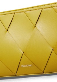 Portafoglio giallo in pelle con una trama intrecciata, caratterizzato dal logo Calvin Klein in bianco. Design compatto con dettagli intricati a motivo diamante.