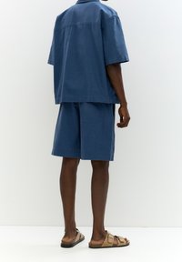 Chemise bleue à manches courtes et short assorti en tissu léger mélangé de coton, offrant une coupe décontractée et un design minimaliste.