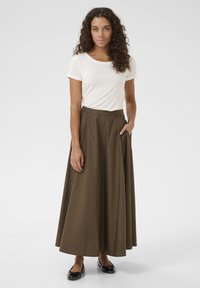 Gonna maxi marrone fluida con tasche laterali, abbinata a una maglietta bianca aderente con maniche corte. Scarpe nere basse completano l'outfit.