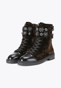 Brown velvet ankle boots with black patent leather toe cap, embellished straps, and decorative studs on the shaft. Rubber sole with textured finish.