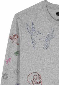 Chemise à manches longues gris clair avec des colibris bleus sur la poitrine, un ange rouge avec des cœurs, un trèfle vert, un flamant rose, un symbole de paix, un soleil et un crâne à contour rouge.