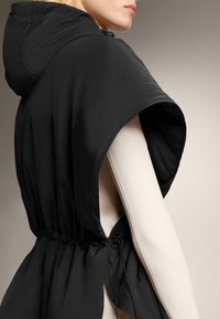 Zwart vest met capuchon en gerimpelde taille, gemaakt van een gladde, lichtgewicht stof met brede armopeningen. Trekkoorddetail aan de zijkant.