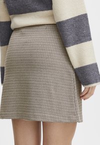 Houndstooth-patterned skirt in beige and brown, made from textured fabric. Features a fitted waist and flared hem, with subtle side slits.