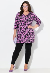 Blommig tunika klänning i svart med rosa blommor, trekvartsärmar, i kombination med svarta leggings och lila högklackade skor.