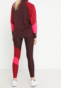 Sudadera granate con acentos rosas, combinada con leggings que presentan un diseño geométrico en granate y rosa. El material parece ser elástico.