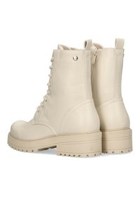 Botas beige hasta el tobillo con punta redonda, cordones en la parte delantera y cremallera lateral. La suela es gruesa con un patrón de tacos. Acentos de herrajes plateados.