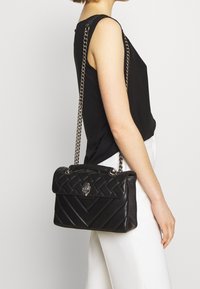 Borsa a mano nera in pelle con motivo trapuntato, tracolla in catena argentata, manico superiore e logo in evidenza sulla parte anteriore. Texture liscia e forma strutturata.