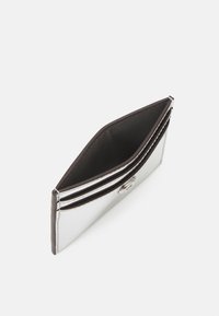 Stříbrný, metalický držák karet s černým interiérem. Obsahuje více přihrádek a uzavření na zapínání. Hladký, lesklý povrch a elegantní design.