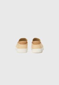 Zapatos slip-on en tono tan con parte superior texturizada y detalles de costura. Suela de goma blanca con acento de logo en el talón. Diseño minimalista.