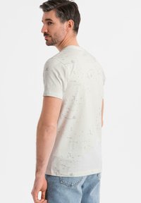 Camiseta de manga corta en gris claro con patrón abstracto de salpicaduras. Tela de algodón suave, corte clásico y cuello redondo sencillo.