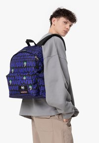 Mochila con tela negra y azul que presenta un patrón repetido de "HA", acentos verdes y detalles de logotipo. Correas ajustables y compartimentos con cremalleras.