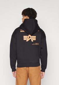 Black hooded sweatshirt made of cotton, featuring an orange logo and text design on the back. Ribbed cuffs and hem with a relaxed fit.