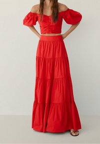 Ensemble rouge deux pièces comprenant un top court à manches épaules dénudées et une jupe longue à volants. Confectionné dans un tissu léger à la texture douce.