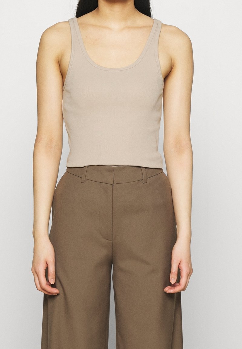 Débardeur ajusté beige en tissu extensible, associé à un pantalon large taille haute marron. Design simple sans motifs visibles.