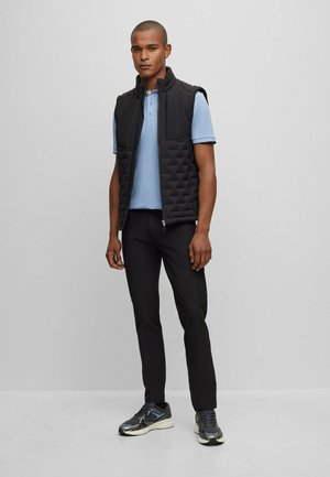 Gilet rembourré noir avec un col haut sur un polo bleu clair. Pantalon noir slim-fit et baskets grises avec des accents réfléchissants.