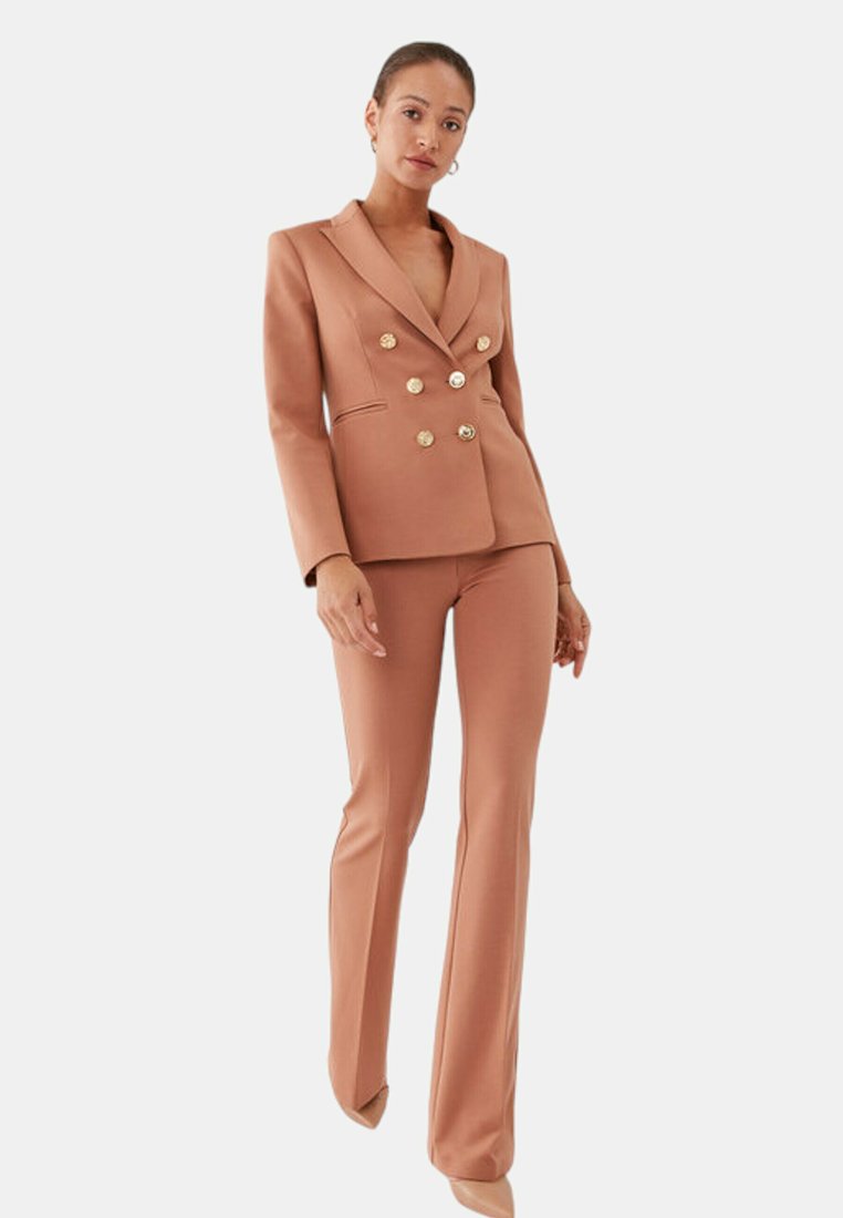 Doppelreiher-Blazer und ausgestellte Hosen aus einem hellbraunen Stoff; mit goldenen Knöpfen und einem maßgeschneiderten Schnitt mit Reverskragen.
