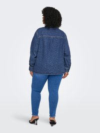 Camicia di denim con vestibilità rilassata, caratterizzata da un motivo screziato, maniche lunghe e piega posteriore. Abbinata a jeans skinny blu e tacchi neri.