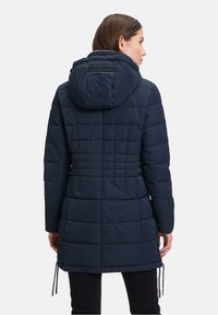 Marineblauwe pufferjas met een capuchon, voorzien van een geborduurd ontwerp, verstelbare touwlijst aan de onderkant en subtiele stikdetails.