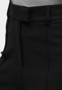 Μαύρο ψηλόμεσο παντελόνι με απαλή υφή, διαθέτει επίπεδη μπροστινή όψη, θηλιές για ζώνη και πλαϊνές τσέπες για λειτουργικότητα.