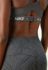 Grauer Sport-BH mit Cut-Out-Design, ausgestattet mit einem breiten Logo-Bund und einer passender, strukturierten Leggings mit einem subtilen Muster.