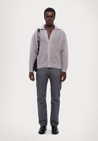 Light gray knitted cardigan with a V-neck and cable pattern, paired with dark gray straight-leg jeans and black shoes.