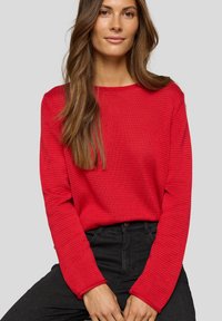 Roter strukturierter Strickpullover mit rundem Halsausschnitt und langen Ärmeln, kombiniert mit schwarzen Hosen. Schlichtes, lässiges Design ohne Verzierungen.