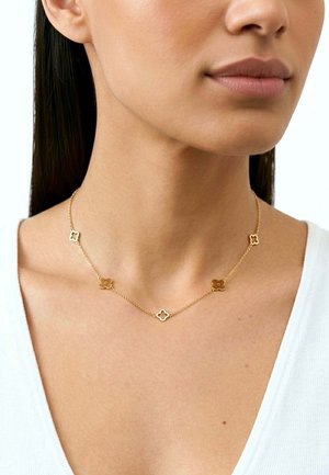 Collana a catena d'oro con maglie a forma di fiore, caratterizzata da un design alternato tra pieno e traforato. Indossata al collo di una modella.