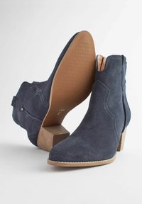 Botine din suede bleumarin, cu vârf ascuțit, toc mic tip bloc și detalii cu cusături pe lateral. Au o talpă texturată din cauciuc.