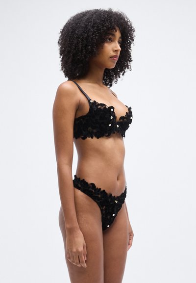 Black lingerie set featuring floral lace design, thin straps, textured fabric, and decorative gold-tone hardware on the bralette and briefs.