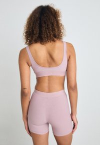 Un reggiseno sportivo rosa chiaro abbinato a pantaloni corti coordinati. Tessuto morbido e elasticizzato, design con schiena a scollo e vita senza cuciture. La vista posteriore mostra la vestibilità e lo stile.