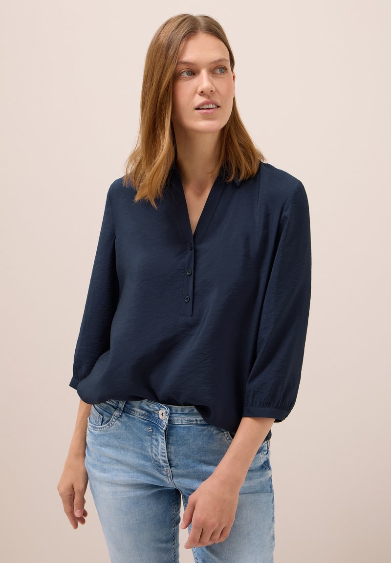 Haut léger bleu marine avec un décolleté en V, trois boutons et des manches 3/4. Tissu texturé avec une coupe décontractée.