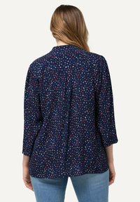 Navy shirt with a printed pattern of small red, white, and blue shapes; features a collar and three-quarter sleeves. Soft fabric texture.