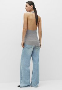 Top halter gri cu spate adânc și model cu buline, asortat cu blugi largi de culoare albastră deschisă și încălțăminte neagră. Textură netedă pe toată suprafața.
