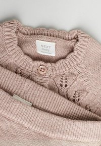 Pull en laine bébé rose clair avec un col rond, fermeture par boutons et motifs de feuilles. Étiquette indiquant "NEXT baby," fabriqué en Chine.