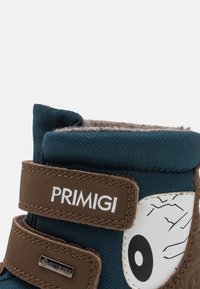 Blaue Stoffstiefel mit zwei braunen Klettverschlüssen, ausgestattet mit einem weißen Augendesign und einem strukturierten Obermaterial, gekennzeichnet mit PRIMIGI- und GORE-TEX-Labels.