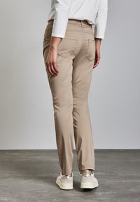 Pantalones de mezcla de algodón beige con un diseño de pierna recta, que cuentan con dos bolsillos traseros y se llevan con zapatillas blancas y plateadas.
