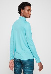 Lichtblauw lange mouwen sporttop met een hoge halslijn, met een gladde textuur en een aansluitend ontwerp. Achteraanzicht zichtbaar.