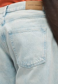 Ανοιχτό μπλε τζιν παντελόνι με πίσω τσέπη που έχει διακοσμητική ραφή και ταμπέλα από ταμπά δέρμα στη μέση.