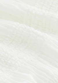 Weißer Stoff mit einem strukturierten Design von gerafften Falten, die sanfte, geschichtete Wellen erzeugen. Das Material wirkt leicht und durchsichtig.